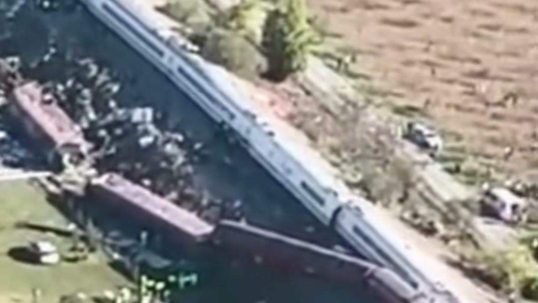 Vista aérea de los dos trenes descarrilados junto a la vía, con los vehículos de emergencia aparcados en el campo de al lado