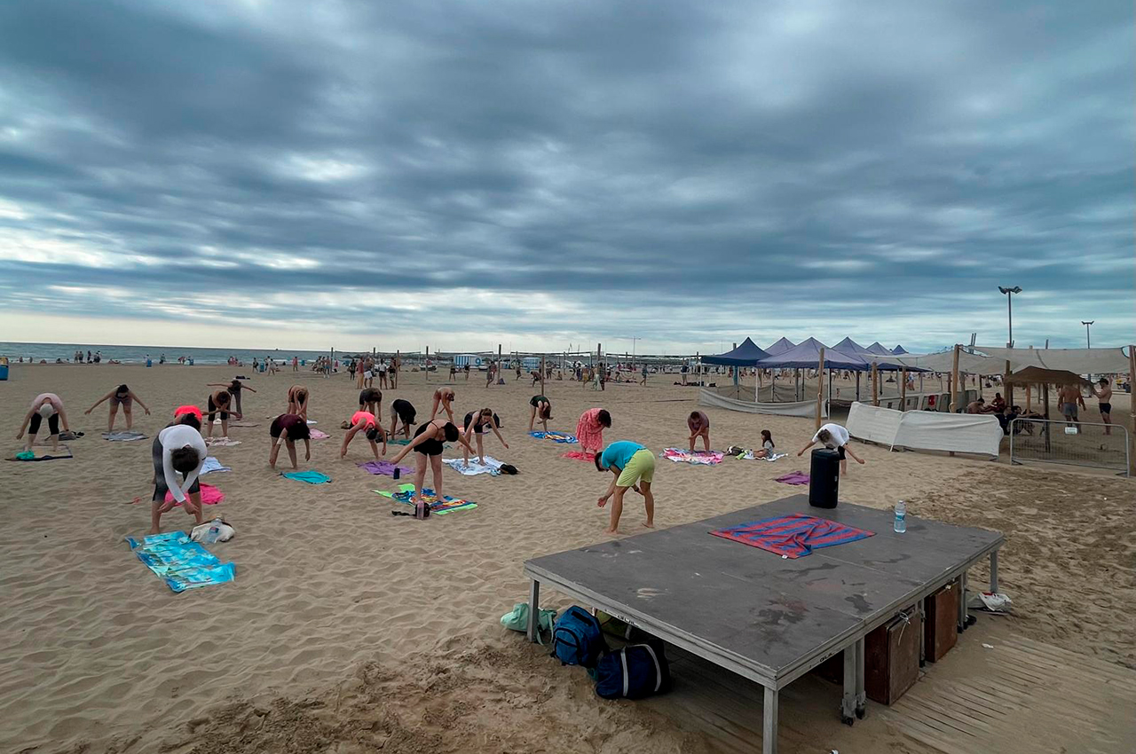 Grupo de personas estirando en la arena durante una clase dirigida gratuita en la playa de la Malva-rosa