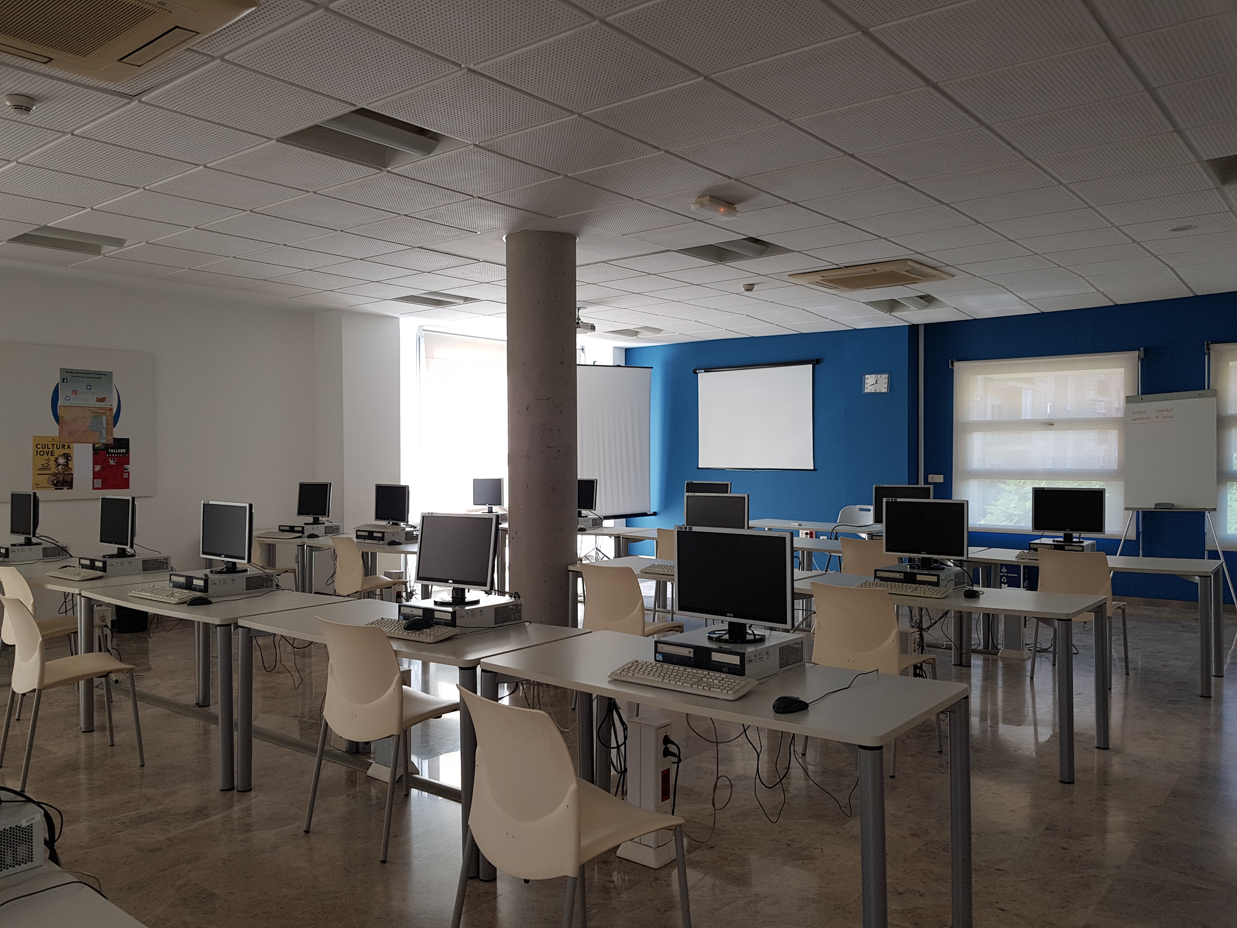 Aula de informática del Espai Jove VLC, con filas de ordenadores, pantalla de proyección y pizarra